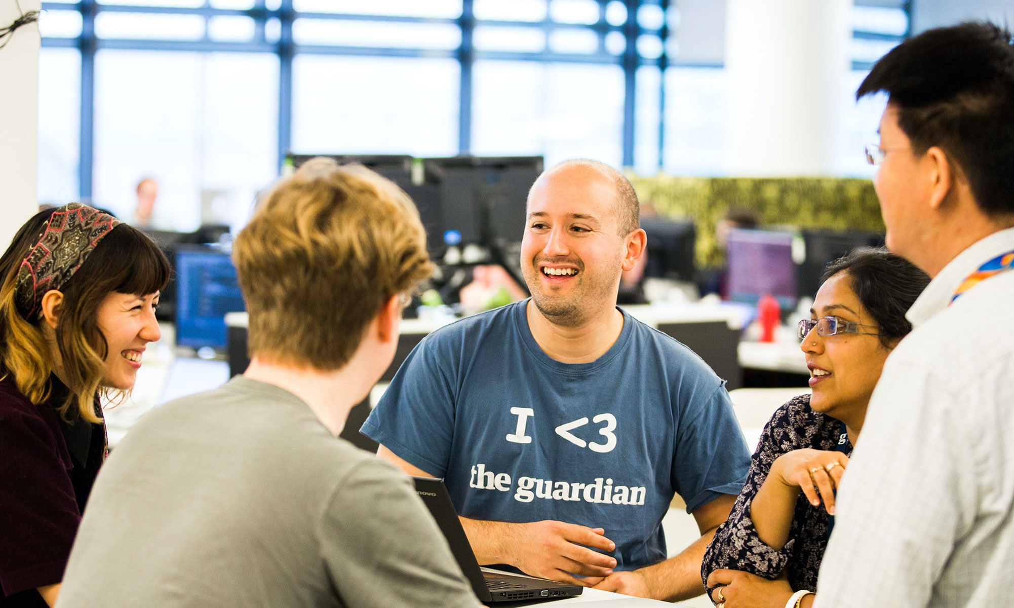 Five people gathered around a table, with a man in the centre wearing an 'I heart the Guardian' tshirt