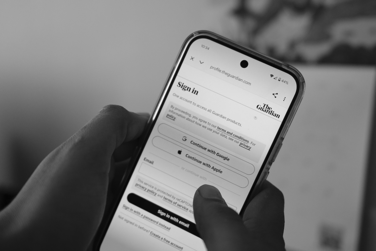 A photograph of a person holding a phone with the Guardian app open, showing the sign-in screen.